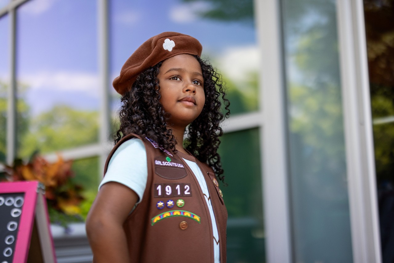 Girl Scout Brownie in uniform standing outside of a building